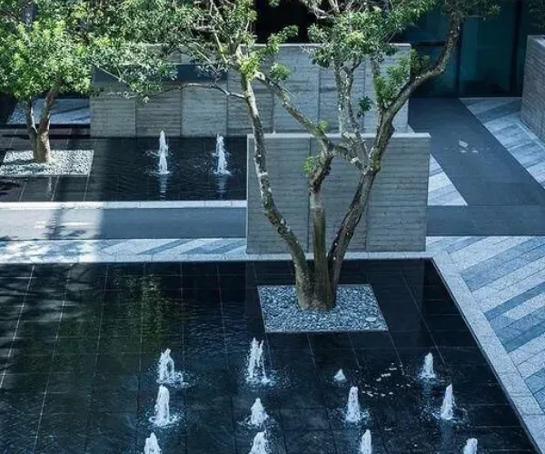 Dark stone reflecting pool with low bubbler jets around a tree planter