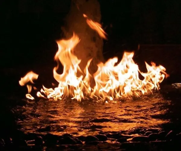 Gas flames burning on the water surface of a dark pebbled basin