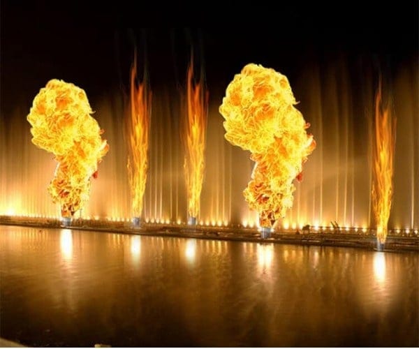 Columns of flame bursting over an illuminated fountain at night