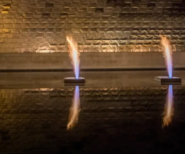 Twin gas flame jets rising from a still dark basin against a stone wall
