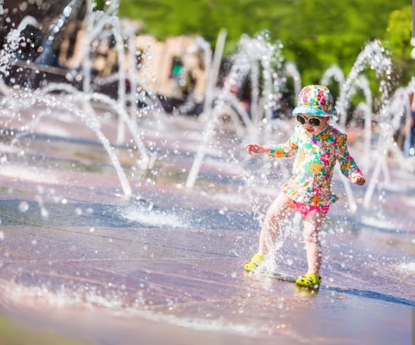 Child playing between low water jets on a plaza