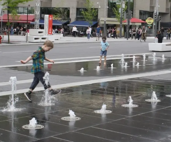 Children running through street-level jets on a city plaza