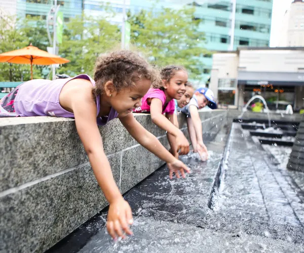 Children reaching over the stone edge of a splash fountain