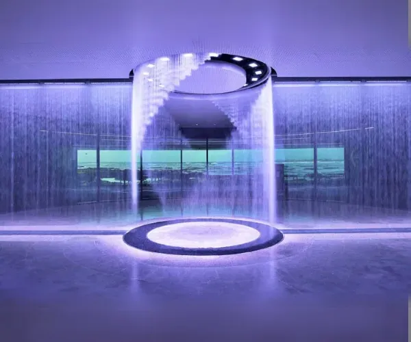Circular rain curtain falling from an oval manifold into a lit ring basin