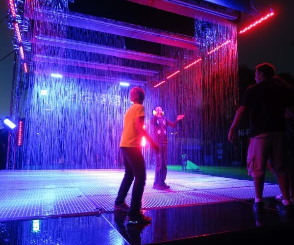 Visitors walking through a purple-lit interactive digital rain room