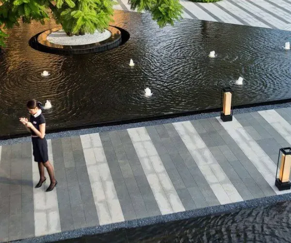 Grade-level black reflecting pool with jets set in striped stone paving