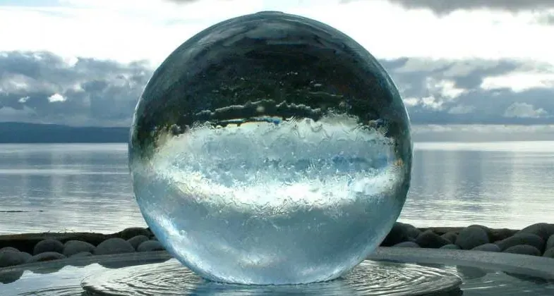 Clear acrylic sphere fountain with a water film over its surface, ocean horizon behind