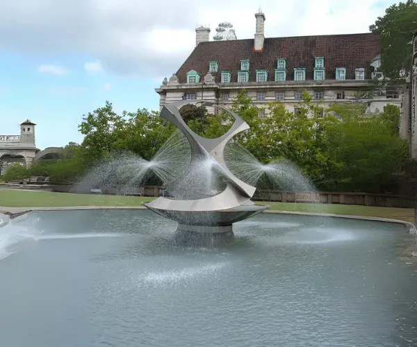 Twisting stainless fountain sculpture over a still pool before a manor house