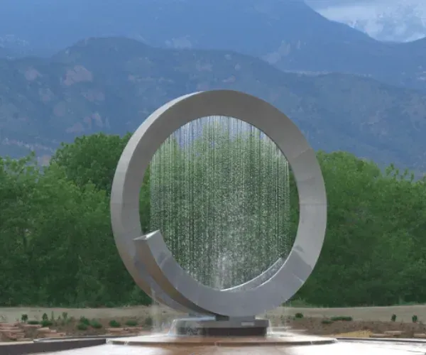 Circular stainless ring sculpture with rain falling inside it, mountains behind
