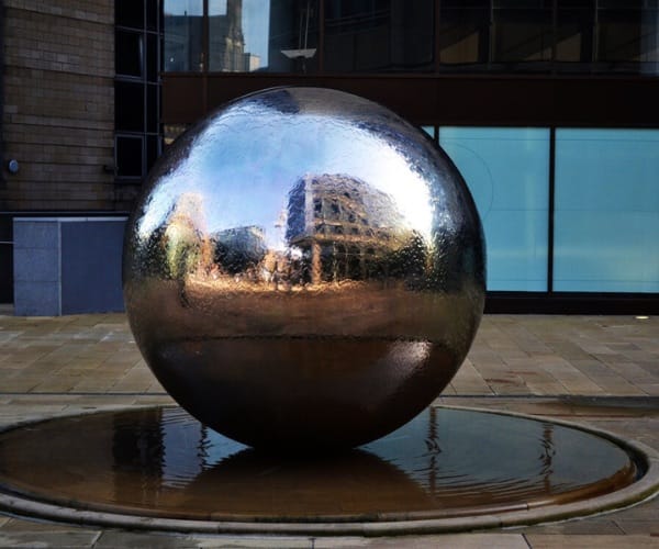Mirror-polished stainless sphere fountain on a stone plaza