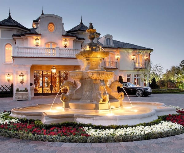 Carved classical fountain lit at night before a mansion