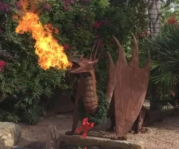 Corten steel dragon sculpture breathing flame in a garden bed