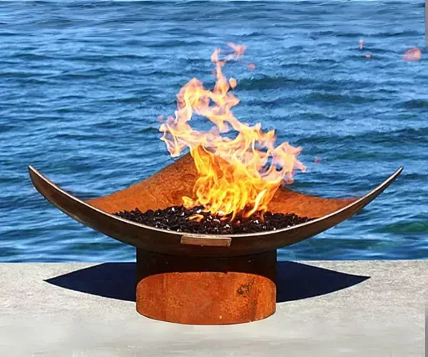 Corten steel crescent fire bowl alight on a round base above open water