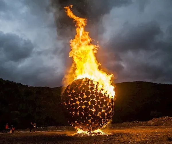 Perforated steel fire sphere burning on a hillside at dusk
