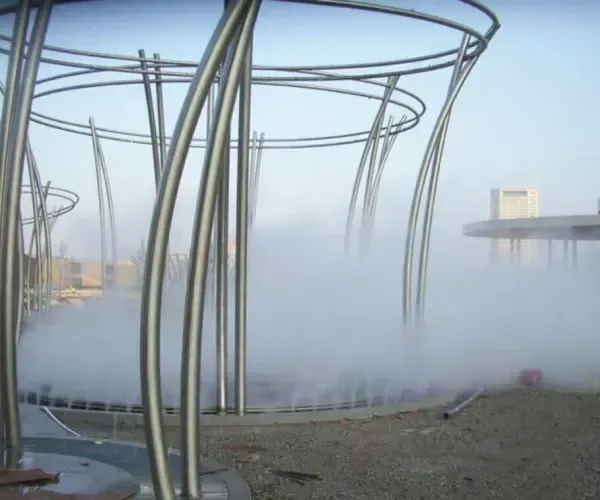Wire-frame columns venting fog beside a waterfront boardwalk