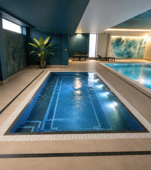 Indoor lap pool in navy mosaic with underwater lights and a potted palm
