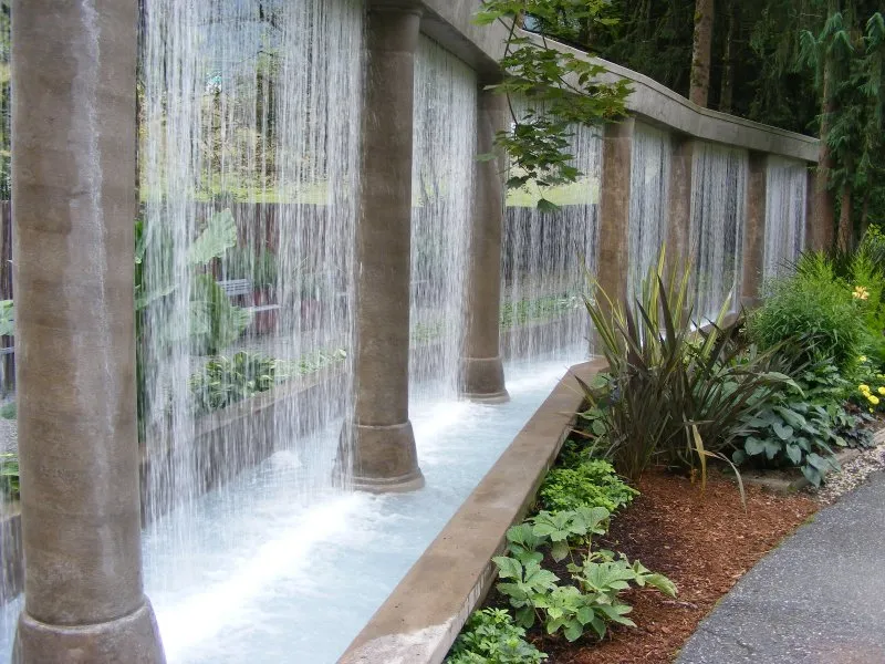 Sheets of water falling between stone columns along a planted garden walk