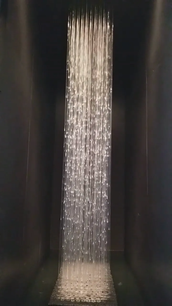 Rain curtain in motion, streams falling into a lit basin