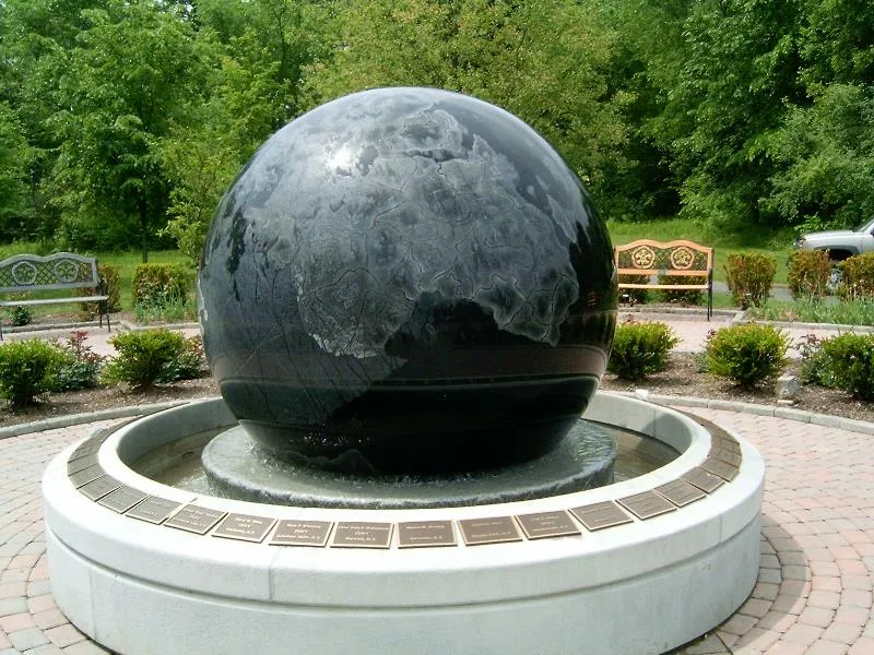 Polished granite globe fountain with carved continents turning on a ring of water in a memorial garden