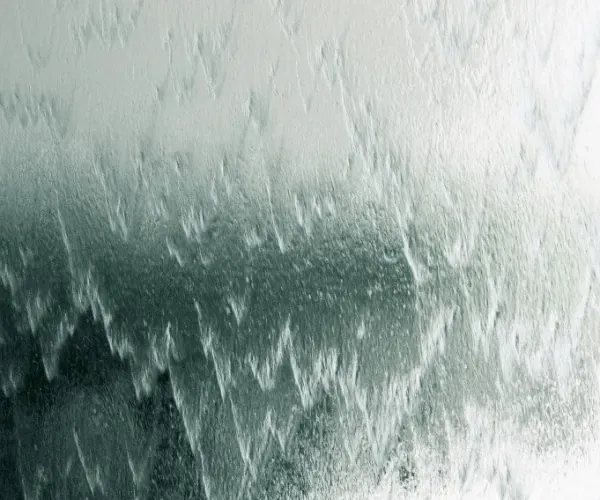 Silver-green chevron ripples of water over textured glass